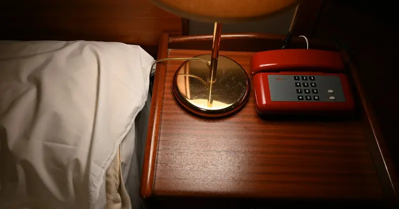 Phone on a nightstand by the bed with the lamp on, a call coming in after hours