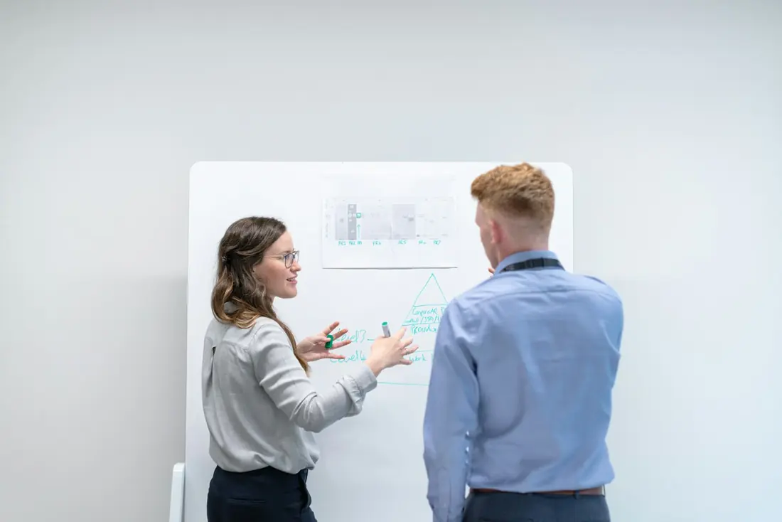 Two colleagues talking through a plan sketched on a whiteboard