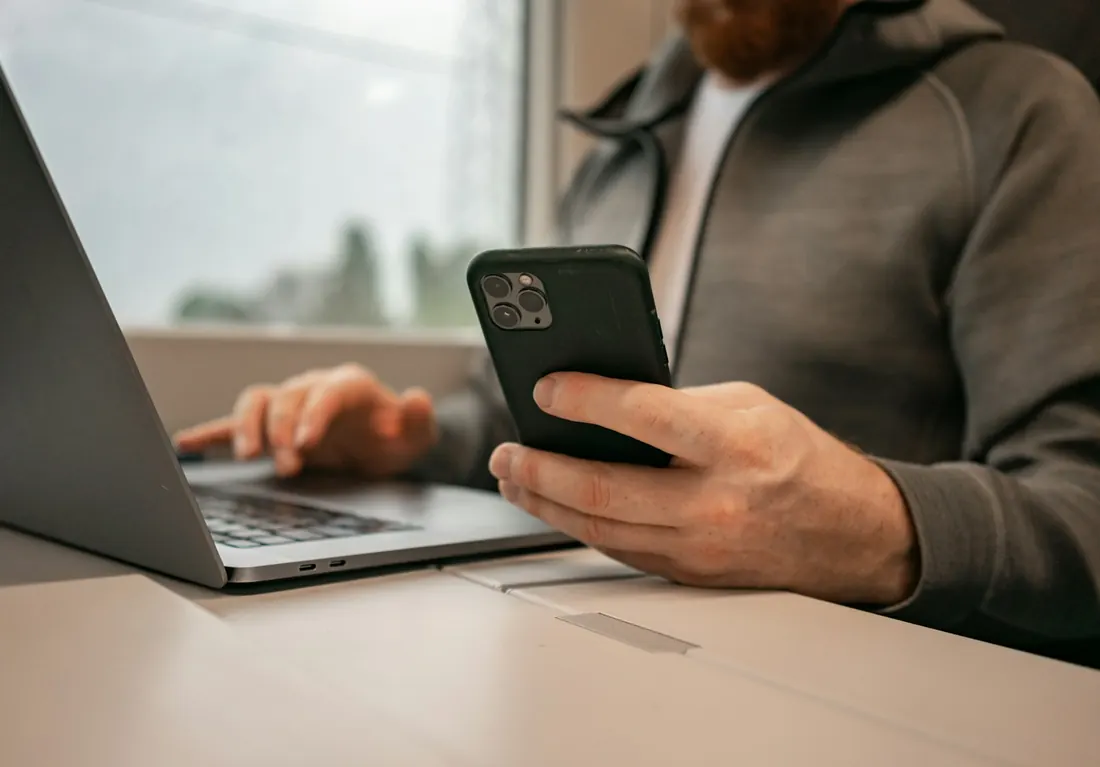 Man checking his phone with a laptop open on the table